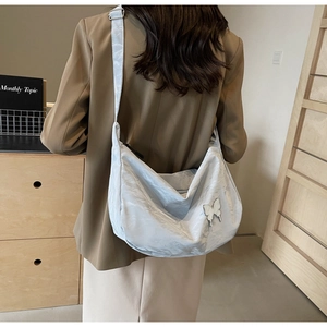 Détail du sac hobo en nylon bleu clair avec emblème papillon argenté et texture plissée