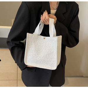 Close-up of embossed floral canvas tote bag with gold buckle held by a model