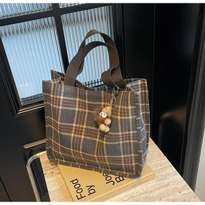 Detail of grey plaid canvas tote bag with brown straps and a plush bear pendant accessory