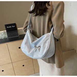Détail du sac hobo bleu texturé orné d'un papillon métallique sur le côté du sac