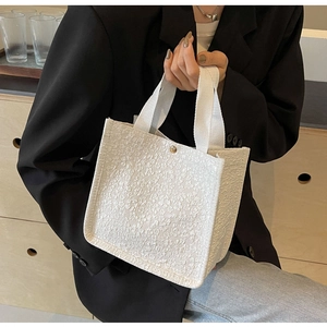 Close-up of white tote bag with floral embossed texture and gold magnetic snap button