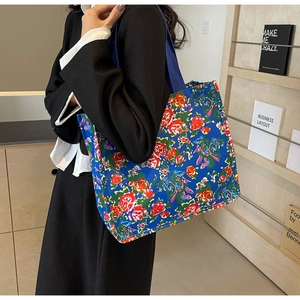 Blue floral canvas tote bag featuring vibrant red roses held by a model in a room