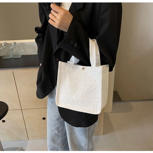Detail of white embossed floral texture and gold button closure on canvas tote bag