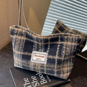 Detail of blue and beige plaid tweed cosmetic bag with fabric label on a dark background