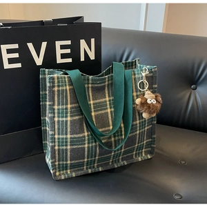 Detail of green and yellow plaid canvas tote bag with a quirky brown plush monster charm