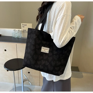 Detail of black canvas tote bag featuring heart embroidery and white woven label