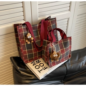 Detail view of large British plaid tote bag set with red web handles and plush monster charm