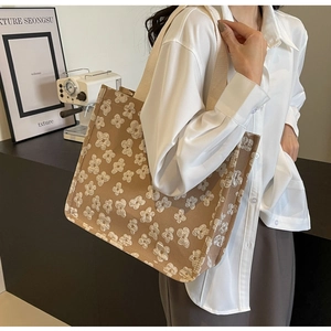 Detail of khaki canvas tote bag featuring white floral embroidery and wide straps
