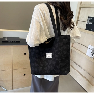Close-up of black heart-embossed tote bag with white branded label on a shoulder strap