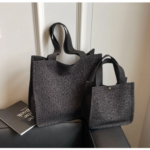 Detail of black tote bag set with embossed floral texture and golden rivet accents