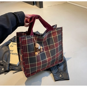 Detail of red and grey plaid canvas tote bag with red strap and plush bear charm