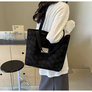 Detail of black canvas tote bag featuring embossed heart patterns and white logo patch