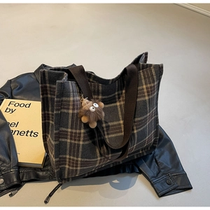Detail of vintage grey plaid tote bag with brown plush monster charm on leather jacket