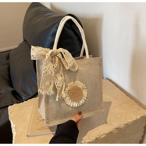 Detail of beige linen handbag with crochet sunflower, lace bow, and cotton rope handles