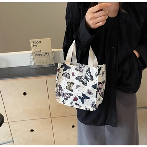 Close-up of a cream canvas tote bag featuring colorful butterfly prints and wide handles
