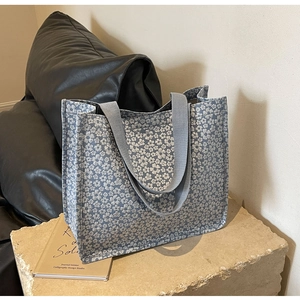 Detail of light blue floral canvas tote bag on stone base with vintage book scene
