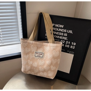 Close-up of beige canvas tote bag with textured white heart embroidery and woven straps