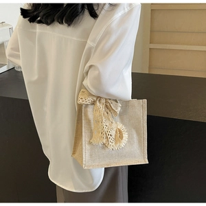 Close-up of beige linen handbag featuring lace bow and sunflower accent on a model