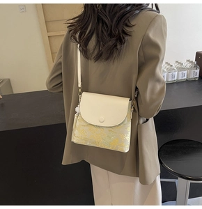 Détail d'un sac bandoulière crème chic avec jacquard floral et pompon blanc décoratif