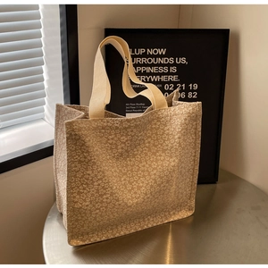 Detail of floral embossed texture and khaki webbing handles on a beige tote bag