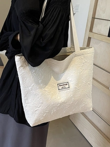 White tote bag with floral texture and woven handle shown on shoulder in wood style setting