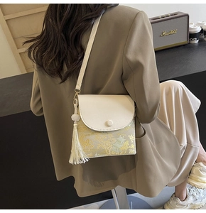 Détail du sac bandoulière beige avec broderie dorée et gland porté par un mannequin rétro