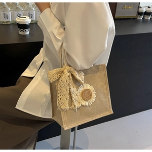 Détail du sac cabas en lin beige avec nœud en dentelle blanche et décor de marguerite
