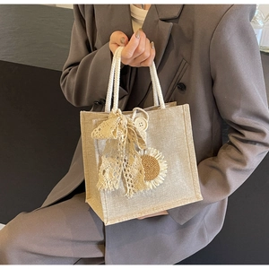 Detail of beige canvas bag featuring a lace bow and embroidered sunflower charm