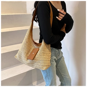 Detail of handwoven straw tote bag featuring herringbone texture and brown leather strap