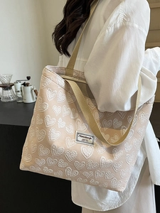 Large beige canvas tote bag with 3D heart patterns shown on a model in a cafe