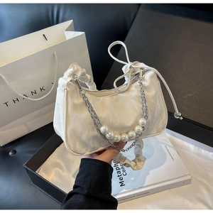 Detail of white pleated underarm bag with silver chain and large pearl strap accents