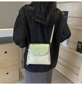 Détail du sac bandoulière vert menthe avec motif doré, pompon blanc et fine lanière