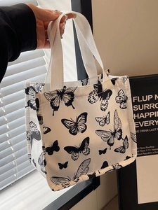 White canvas tote bag featuring black butterfly prints with woven top handles