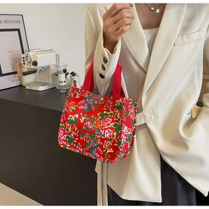 Détail d'un sac cabas rouge en toile fleurie tenu par un mannequin dans un café chic
