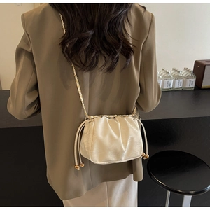 Close-up of a beige pleated cloud bag featuring gold ball drawstring and chain strap detail