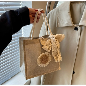 Sac fourre-tout en lin avec patch tournesol et nœud en dentelle tenu devant un trench