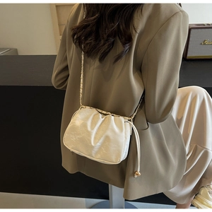 Detail of white pleated cloud bag with golden chain strap and spherical pendant