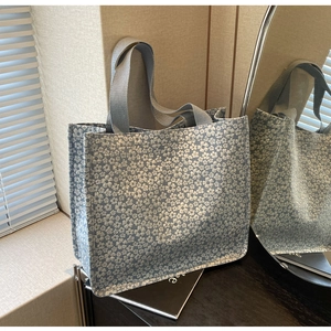Detail of light blue tote bag with silver floral texture and grey canvas handles on wood