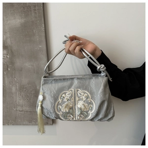 Détail d'un sac en soie argentée avec broderie florale et accessoire à pompon blanc