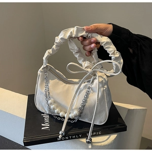 Detail of white pleated underarm bag with pearl chain decoration and ribbon bow