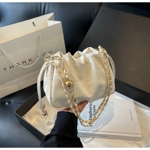 Detail of white dumpling bag with adjustable gold ball chain strap on gift box