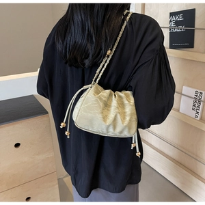 Detail of light green ruched shoulder bag featuring drawstring with gold ball charm