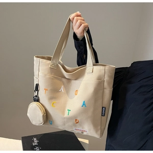 Détail du sac fourre-tout en toile beige avec broderie et mini pochette attachée