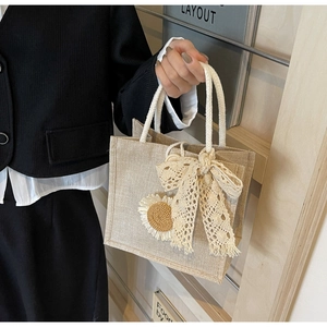 Détail d'un sac cabas en jute tressé avec nœud en dentelle et décoration de tournesol