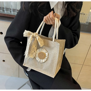 Détail du sac tissé beige avec poignées en corde blanche et marguerite en dentelle décorative