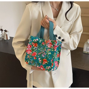 Detailed texture of a floral canvas handbag in dark green with blue handles