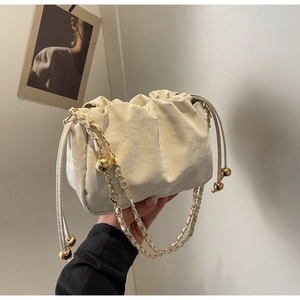 Detail of cream pleated cloud bag with gold drawstring beads and woven chain strap