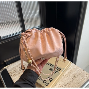 Close-up of pink ruched cloud bag with glossy fabric and gold chain with ball charm