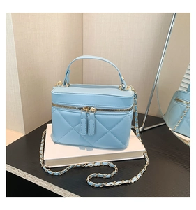 Close-up of light blue quilted box bag with gold double zippers and chain strap detail