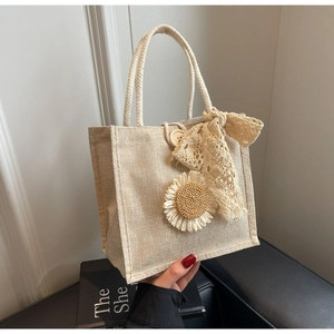 Détail d'un sac à main en lin beige avec fleur au crochet, nœud et bouton en bois